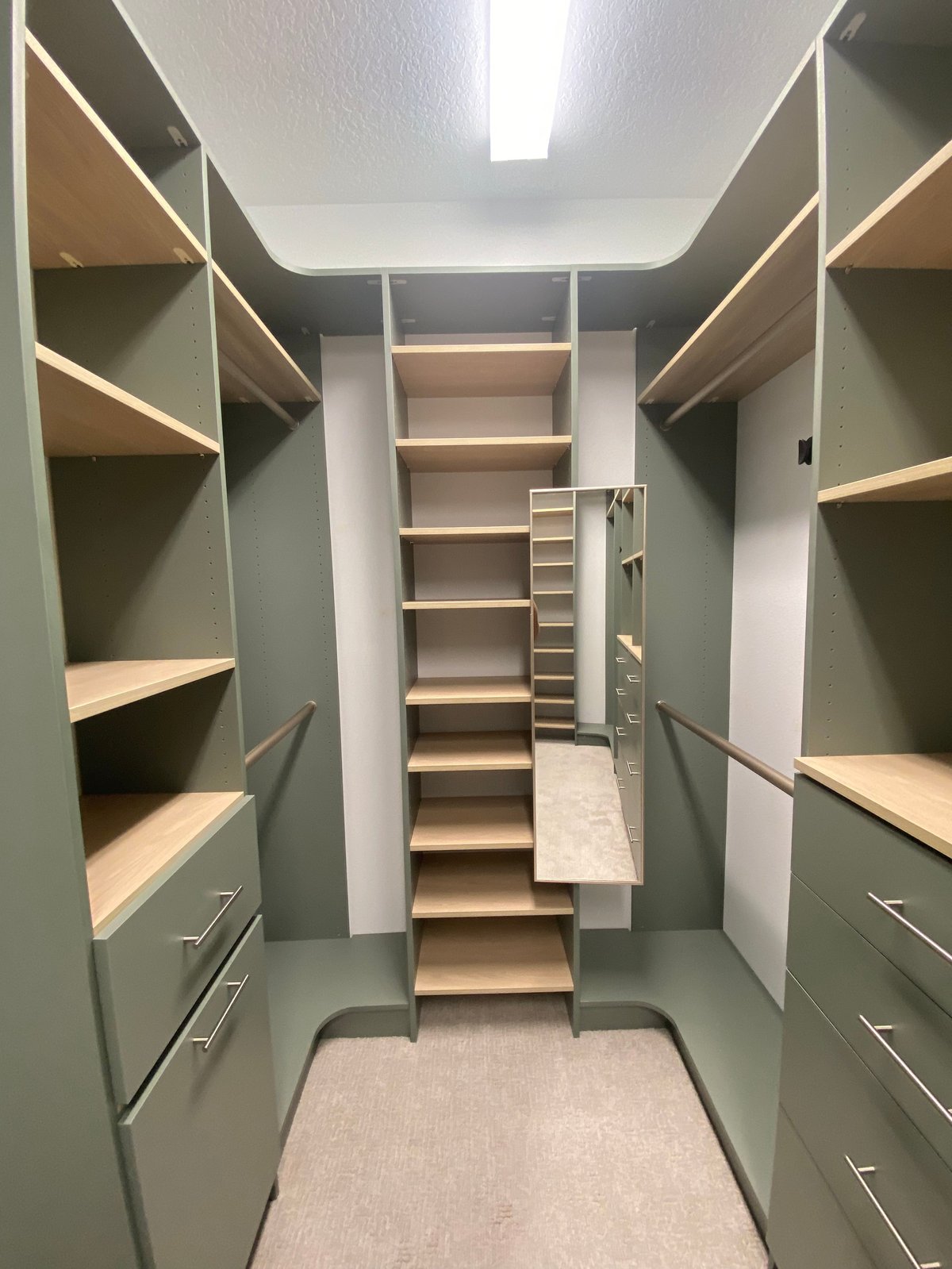 Modern walk-in closet with sage green walls, built-in shelving, wooden shelves, drawers, and a central staircase leading upward