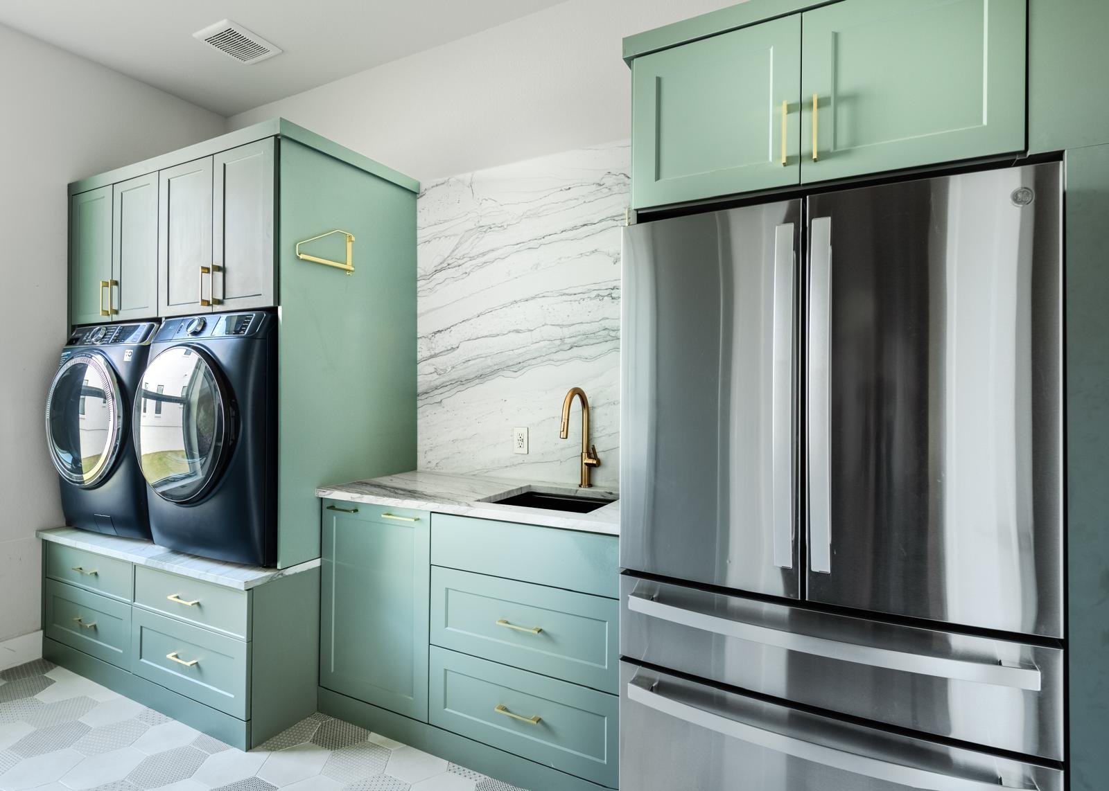 Modern kitchen with sage green cabinetry, marble backsplash, stainless steel appliances, and integrated laundry area with front-load washers and dryers
